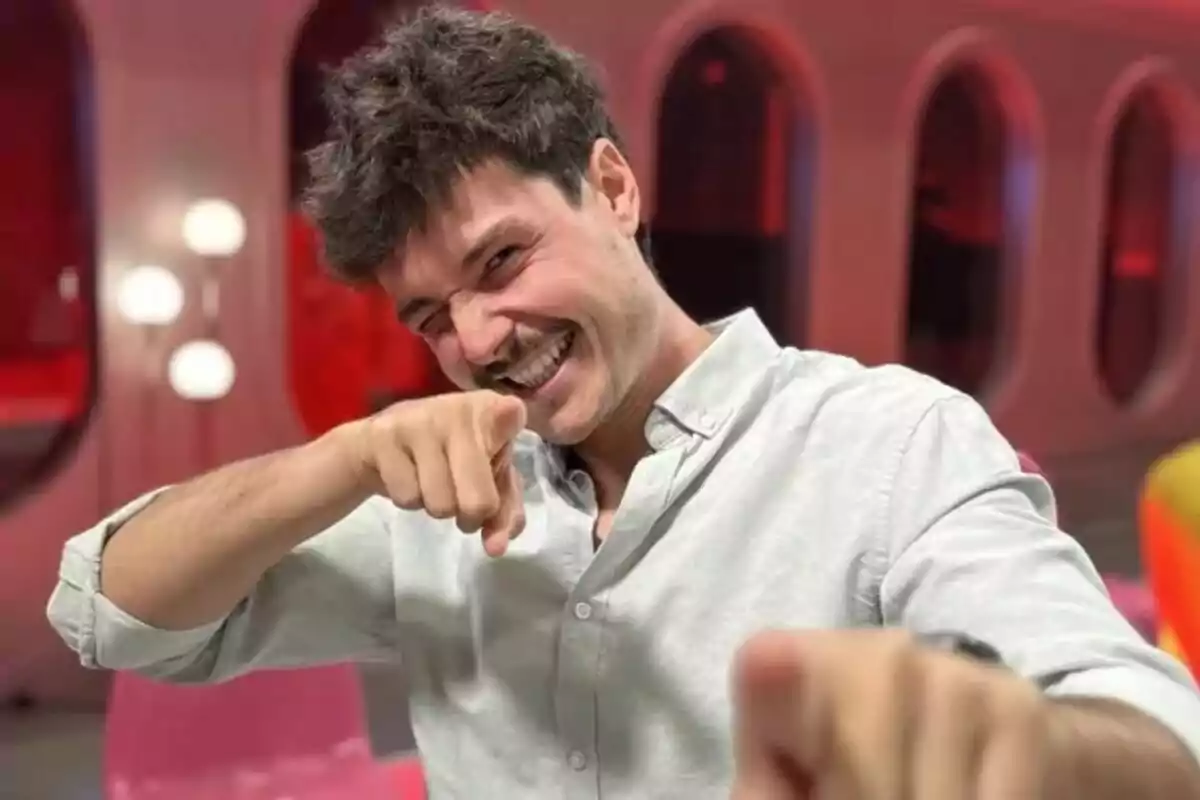 Miki Núñez somrient amb bigoti i camisa clara apunta cap a la càmera en un ambient amb llums i tons vermells. Miki Núñez somrient amb bigoti i camisa clara apunta cap a la càmera en un ambient amb llums i tons vermells.