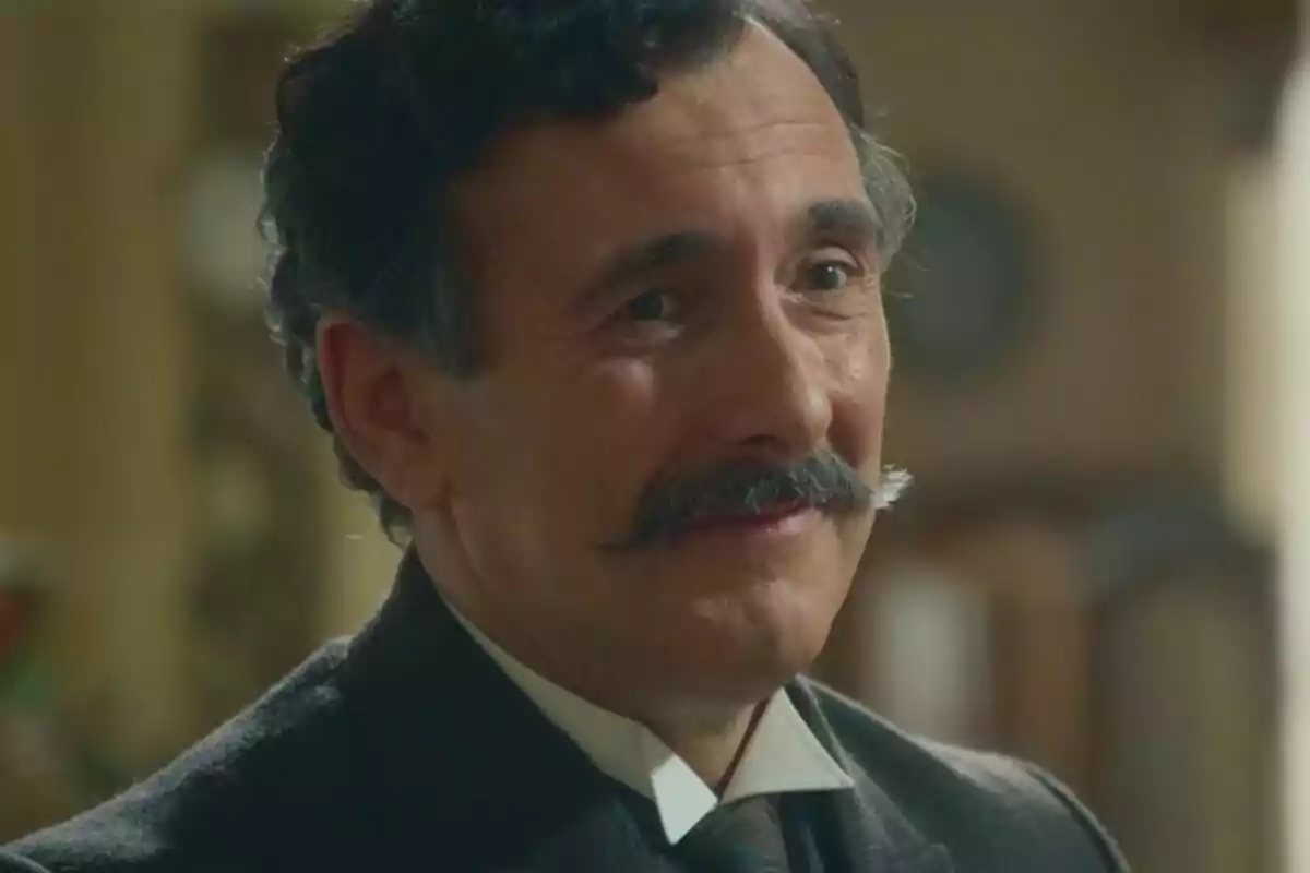 Miquel García Borda con bigote y cabello oscuro sonríe mientras lleva un traje formal en La Promesa. Miquel García Borda con bigote y cabello oscuro sonríe mientras lleva un traje formal en La Promesa.