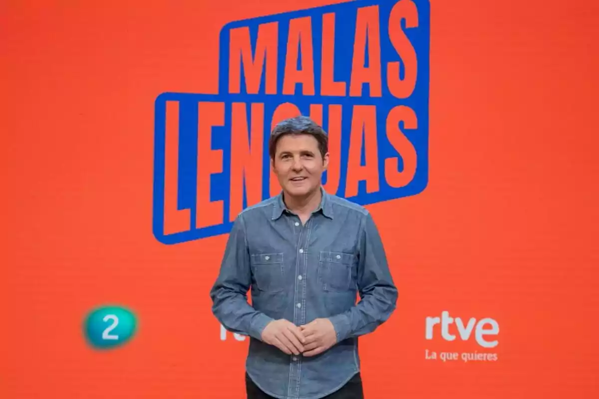 Jesús Cintora con camisa de mezclilla está de pie frente a un fondo rojo con el texto 