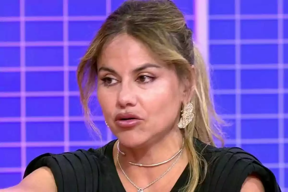 Mónica Hoyos amb cabell recollit i arracades grans en un plató de televisió amb fons blau quadriculat a Tardear.
