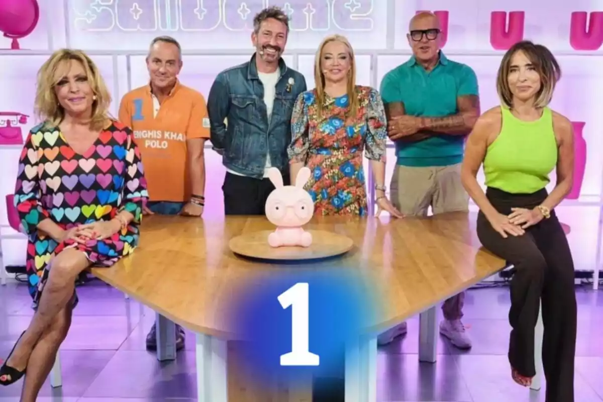 Un grupo de personas posando alrededor de una mesa de madera con un objeto decorativo en el centro y un número uno en la parte inferior. Un grupo de personas posando alrededor de una mesa de madera con un objeto decorativo en el centro y un número uno en la parte inferior.