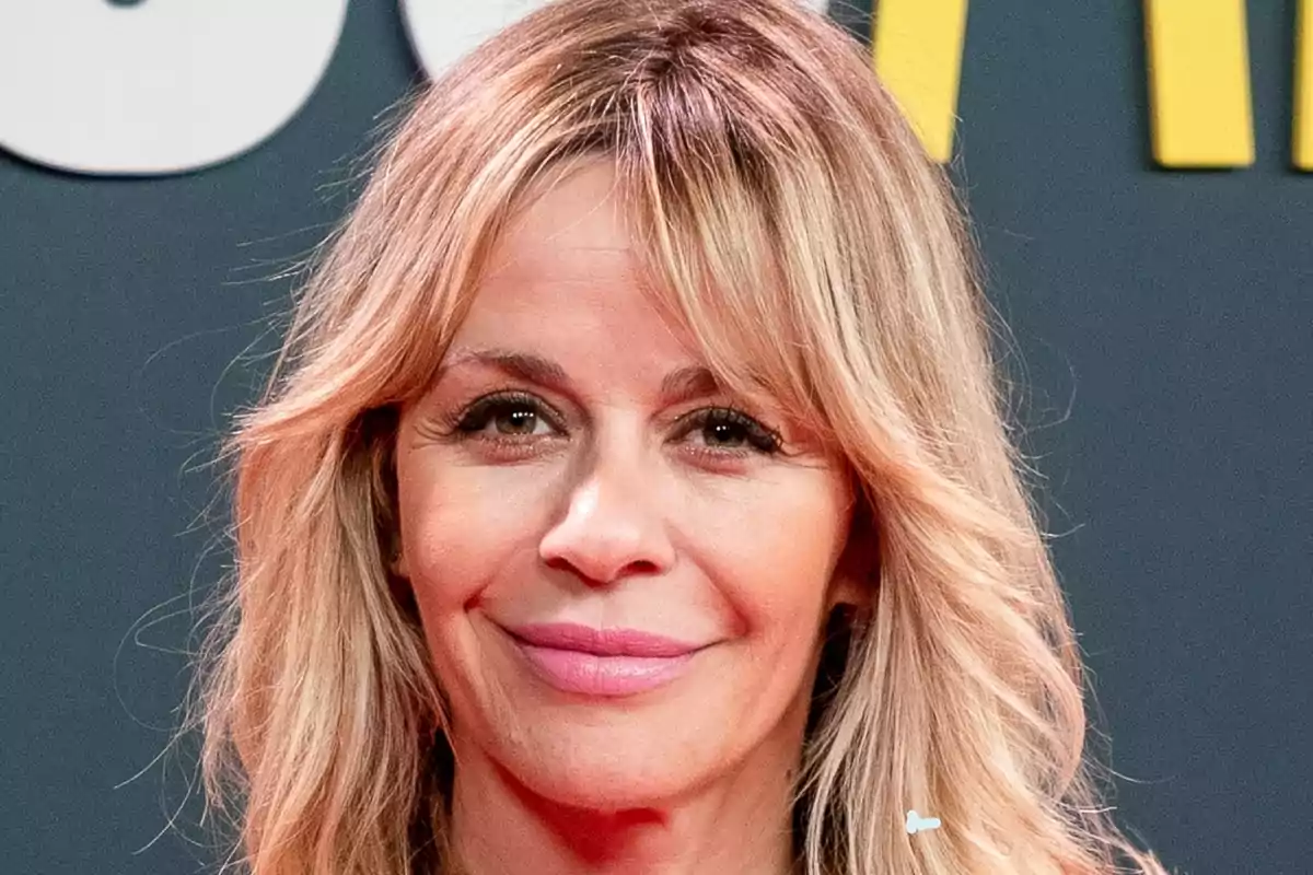 María Adánez sonriendo frente a una pared gris con letras blancas y amarillas. María Adánez sonriendo frente a una pared gris con letras blancas y amarillas.