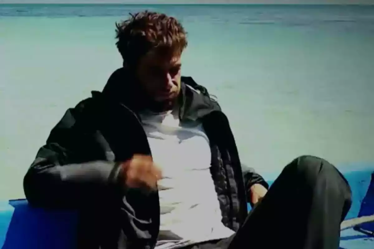 Montoya sentado en una silla azul junto al mar con una chaqueta negra y camiseta blanca en Supervivientes.
