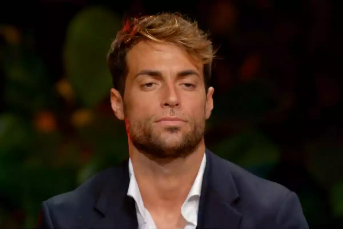 Montoya con barba y cabello castaño claro, vistiendo un traje oscuro y camisa blanca, con expresión seria y fondo desenfocado en La Isla de las Tentaciones. Montoya con barba y cabello castaño claro, vistiendo un traje oscuro y camisa blanca, con expresión seria y fondo desenfocado en La Isla de las Tentaciones.