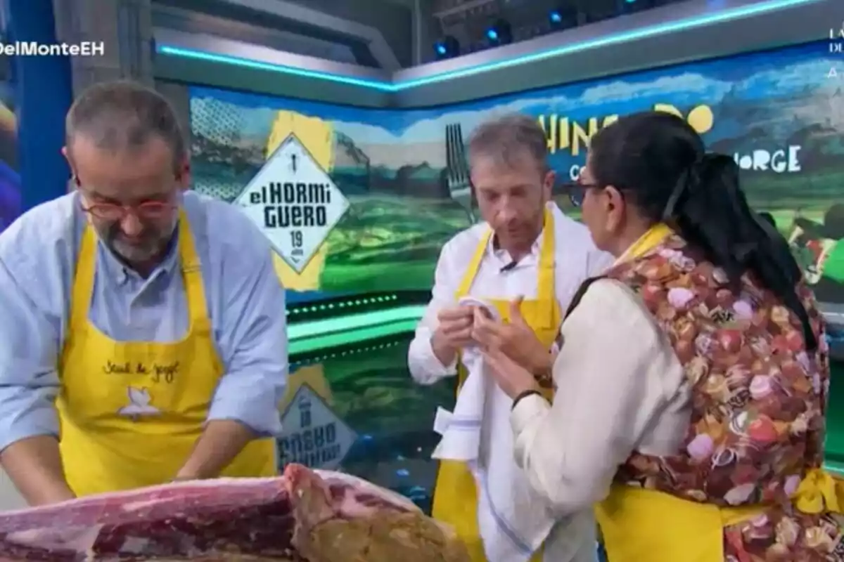 David de Jorge, María del Monte y Pablo Motos con delantales amarillos está en 'El Hormiguero', aparentemente participando en una actividad culinaria, mientras una gran pieza de carne está sobre la mesa frente a ellos. David de Jorge, María del Monte y Pablo Motos con delantales amarillos está en 'El Hormiguero', aparentemente participando en una actividad culinaria, mientras una gran pieza de carne está sobre la mesa frente a ellos.