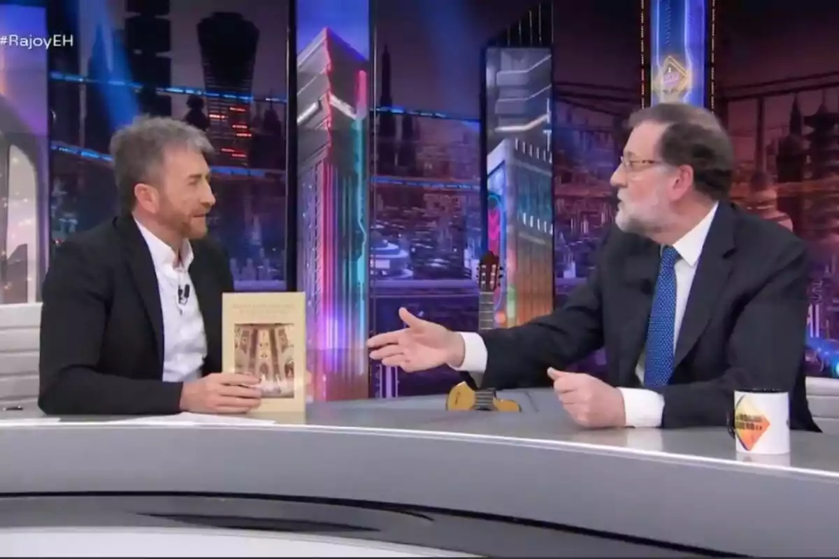 Maríano Rajoy i Pablo Motos conversen en un plató de televisió modern; un sosté un llibre mentre l'altre estén la mà a 'El Hormiguero'. Maríano Rajoy i Pablo Motos conversen en un plató de televisió modern; un sosté un llibre mentre l'altre estén la mà a 'El Hormiguero'.