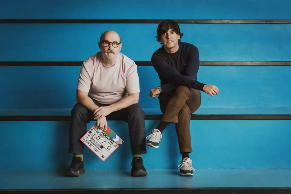 Javier Cámara y Diego San José sentados en unas gradas azules una de ellas sostiene una claqueta de cine.