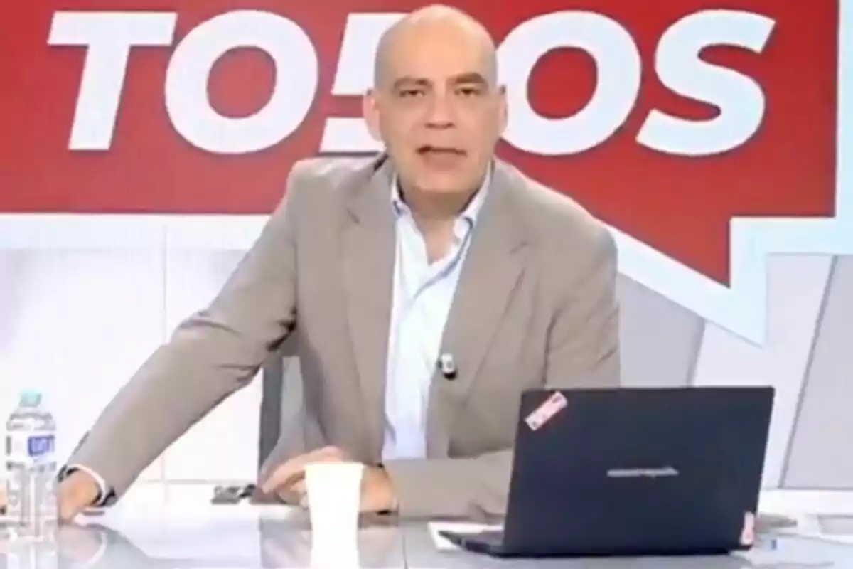 Nacho Abad amb vestit clar està assegut en un escriptori amb un portàtil i una ampolla d'aigua, davant d'un fons vermell amb lletres blanques a 'En boca de todos'. Nacho Abad amb vestit clar està assegut en un escriptori amb un portàtil i una ampolla d'aigua, davant d'un fons vermell amb lletres blanques a 'En boca de todos'.