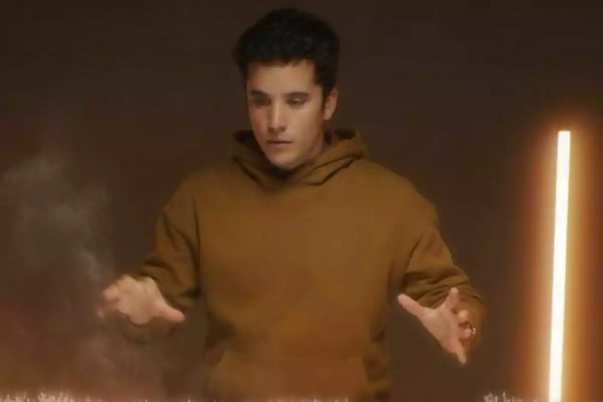 Emilio Doménech con sudadera marrón parece concentrado mientras extiende las manos frente a una luz vertical en un ambiente oscuro en Gabinete de Crisis.