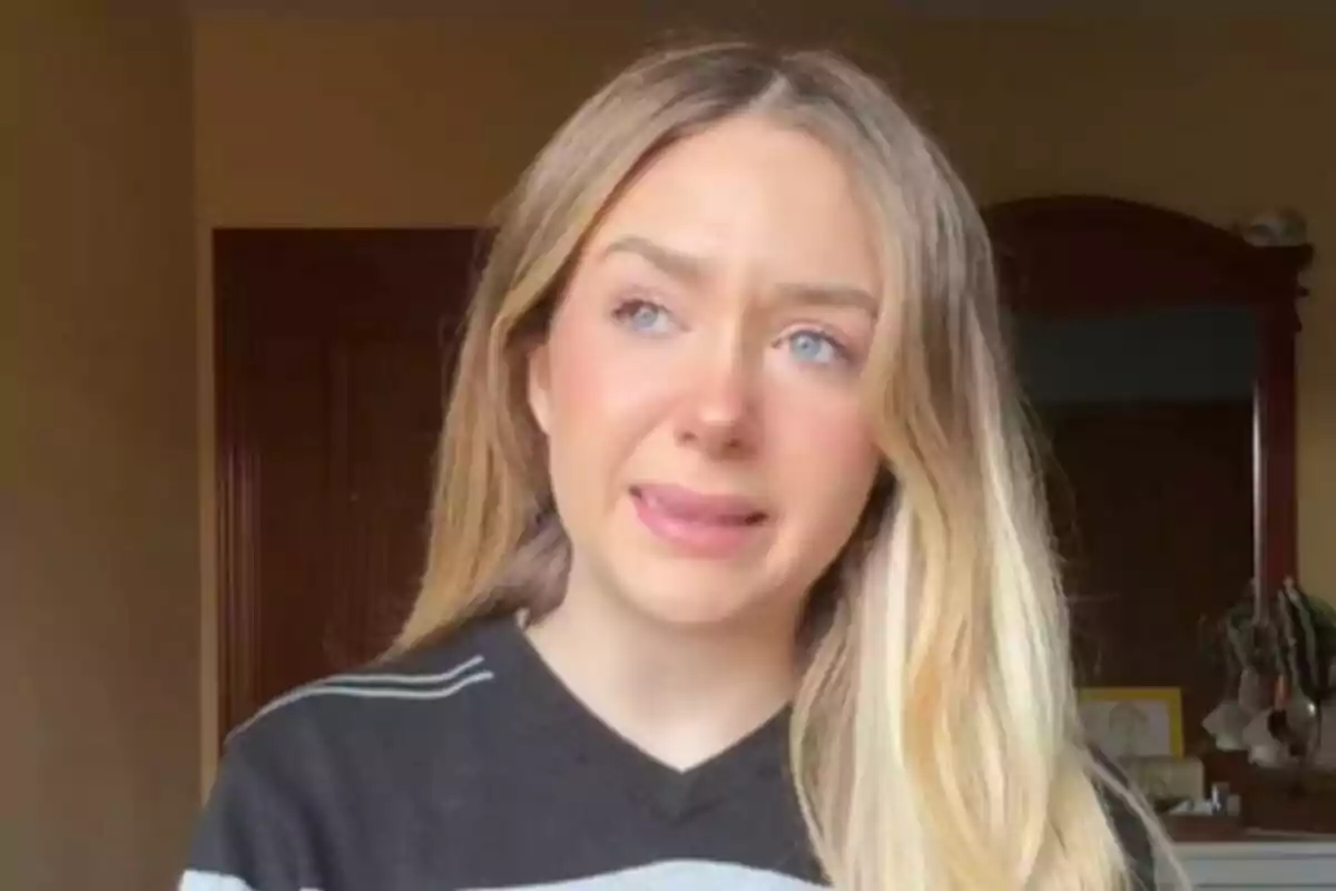 Natalia Jiménez amb cabell ros i solt, vestint un suèter fosc amb ratlles, sembla estar emocionada o plorant en una habitació amb parets de color clar.
