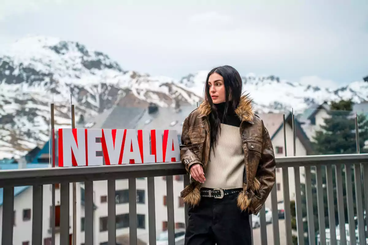 Natalia Lacunza amb jaqueta de pell sintètica i jersei clar està dreta al costat d'un rètol que diu "NEVALIA" amb un paisatge muntanyós nevat de fons.