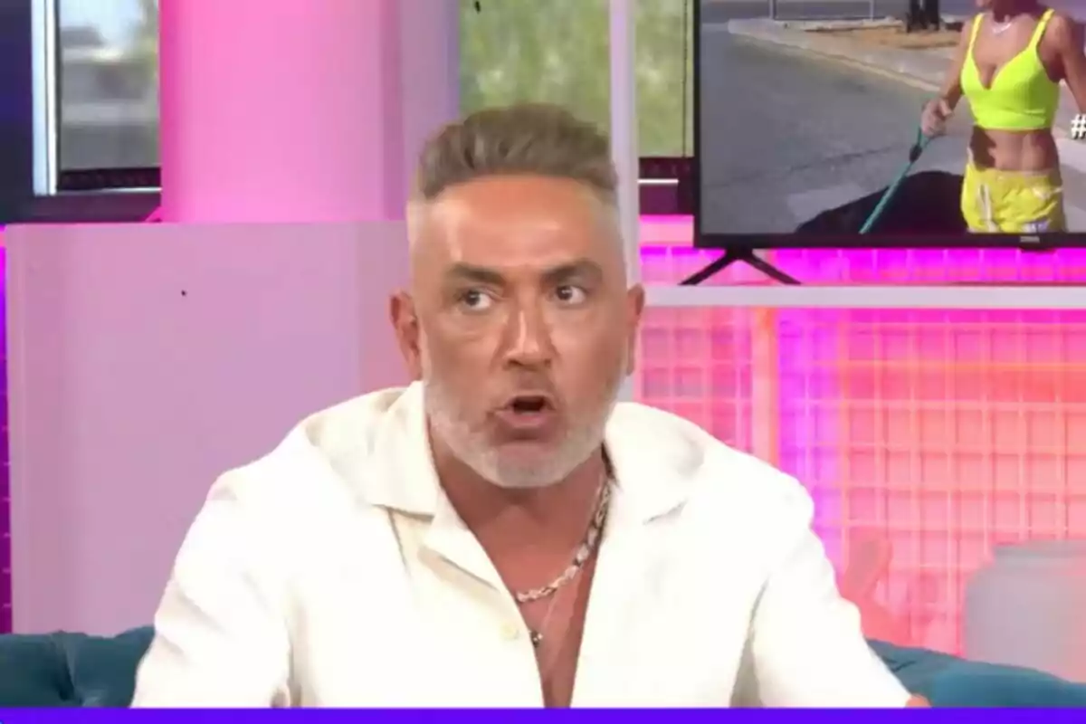 Kiko Hernández con camisa blanca y cabello corto hablando en 'Ni que fuéramos' con fondo rosa y pantalla mostrando a una mujer en ropa deportiva.