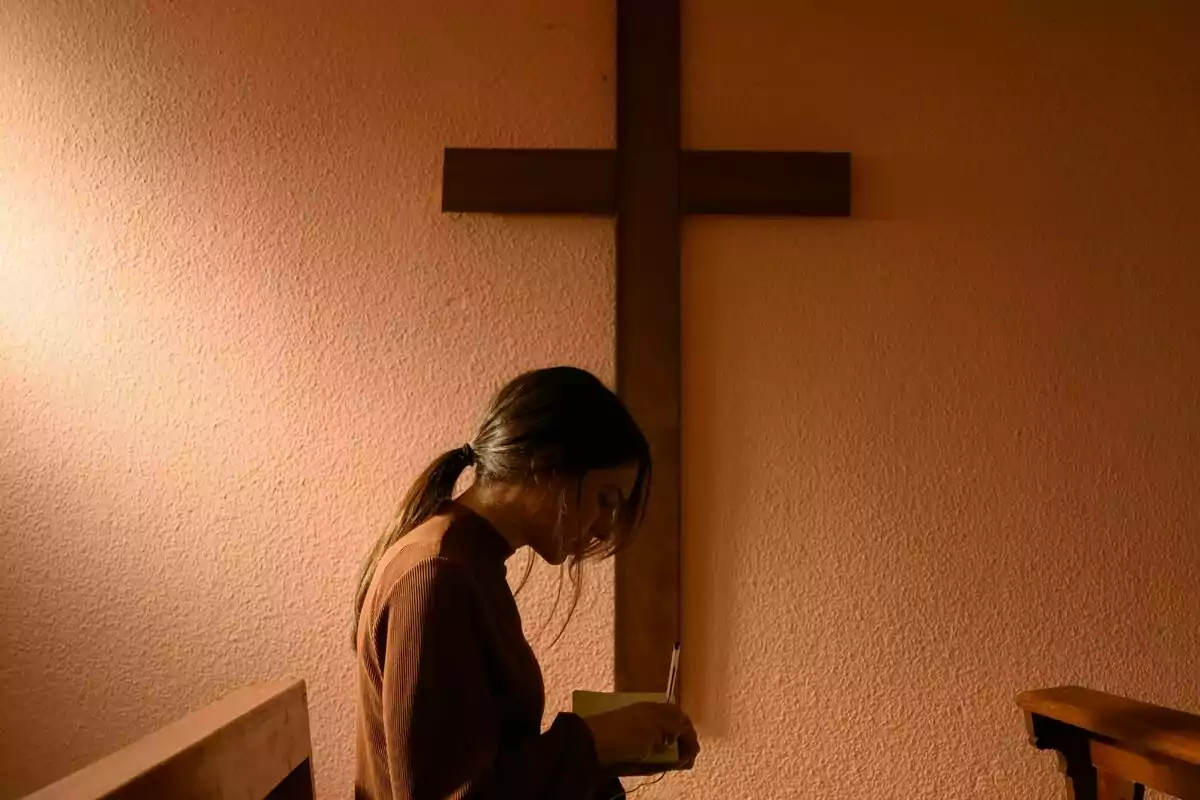 Claudia Traisac escrivint en un quadern en una habitació amb una creu de fusta a la paret a El minut heroic: Jo també vaig deixar l'Opus Dei. Claudia Traisac escrivint en un quadern en una habitació amb una creu de fusta a la paret a El minut heroic: Jo també vaig deixar l'Opus Dei.