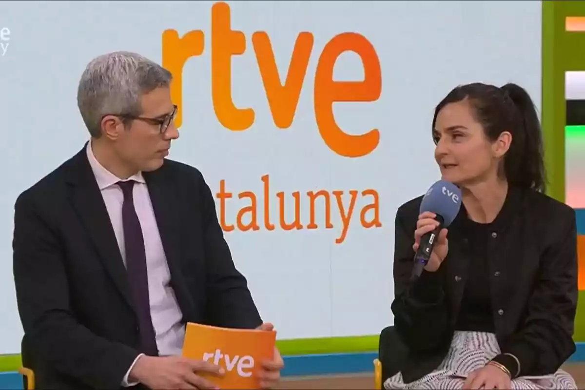 Oriol Nolis y Laura Folguera están sentadas en un set de televisión de RTVE Catalunya, una de ellas sostiene un micrófono mientras conversan en la presentación de 2Cat.