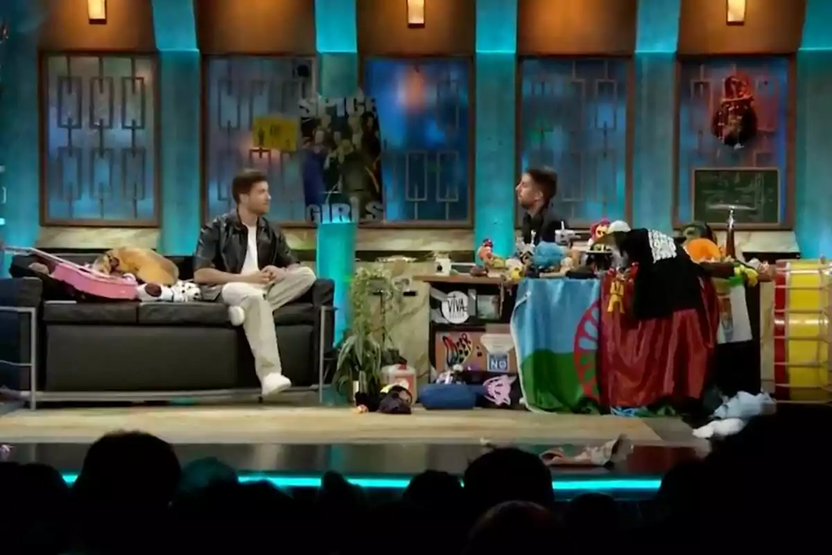 'La Revuelta' con Pablo Alborán y David Broncano conversando en un set desordenado lleno de objetos variados y un perro descansando en un sofá. 'La Revuelta' con Pablo Alborán y David Broncano conversando en un set desordenado lleno de objetos variados y un perro descansando en un sofá.