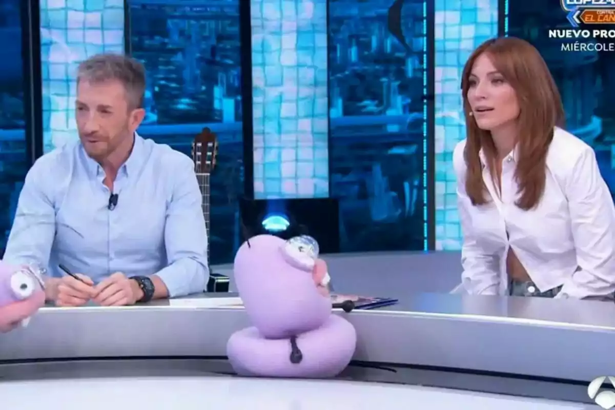 Pablo Motos al costat d'Edurne assegudes al plató del Hormiguero amb marionetes morades sobre la taula. Pablo Motos al costat d'Edurne assegudes al plató del Hormiguero amb marionetes morades sobre la taula.