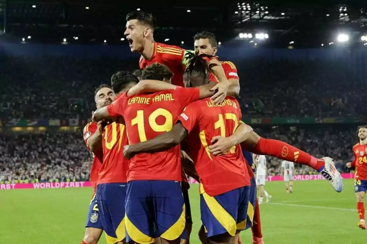 Jugadores de fútbol con uniformes rojos y amarillos celebran un gol en un estadio lleno de espectadores. Jugadores de fútbol con uniformes rojos y amarillos celebran un gol en un estadio lleno de espectadores.
