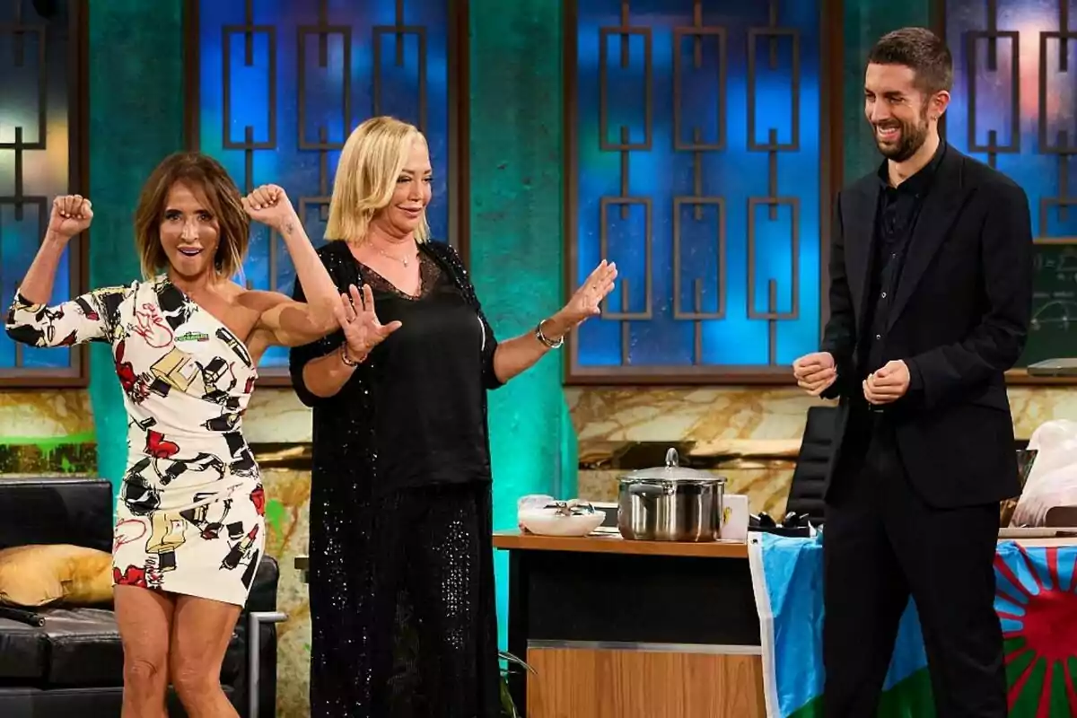 Tres personas en La Revuelta, María Patiño, Belén Esteban y David Broncano, están sonriendo y haciendo gestos con las manos, mientras una olla y una bandera están sobre una mesa cercana. Tres personas en La Revuelta, María Patiño, Belén Esteban y David Broncano, están sonriendo y haciendo gestos con las manos, mientras una olla y una bandera están sobre una mesa cercana.