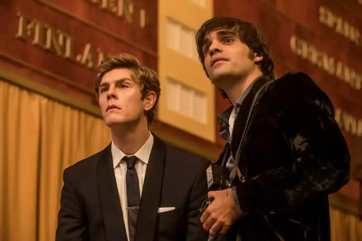 Patrick Criado y Alex Brendemühl formalmente observan algo con atención en un ambiente interior elegante en la serie La Canción. Patrick Criado y Alex Brendemühl formalmente observan algo con atención en un ambiente interior elegante en la serie La Canción.