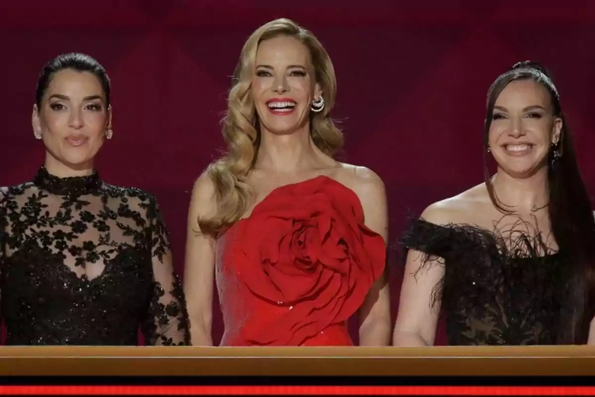 Ruth Lorenzo, Paula Vázquez e Inés Hernand posan juntas en un evento, vestidas elegantemente con vestidos de gala en tonos oscuros y rojo, sobre un fondo rojo en la semifinal del Benidorm Fest.