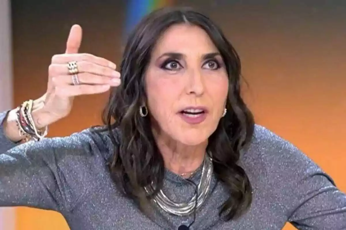 Pau Padilla amb cabell fosc i arrissat, vestint una brusa brillant i accessoris, gesticula amb la mà aixecada al plató de TardeAR. Pau Padilla amb cabell fosc i arrissat, vestint una brusa brillant i accessoris, gesticula amb la mà aixecada al plató de TardeAR.