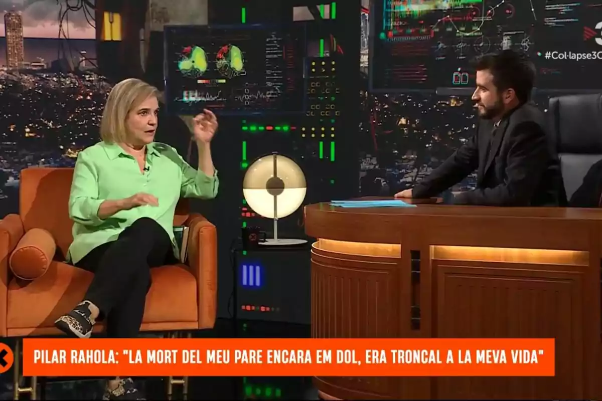 Pilar Rahola amb brusa verda està asseguda en una butaca taronja mentre conversa amb Ricard Ustrell de vestit fosc al plató de Col·lapse amb pantalles i llums de fons. Pilar Rahola amb brusa verda està asseguda en una butaca taronja mentre conversa amb Ricard Ustrell de vestit fosc al plató de Col·lapse amb pantalles i llums de fons.