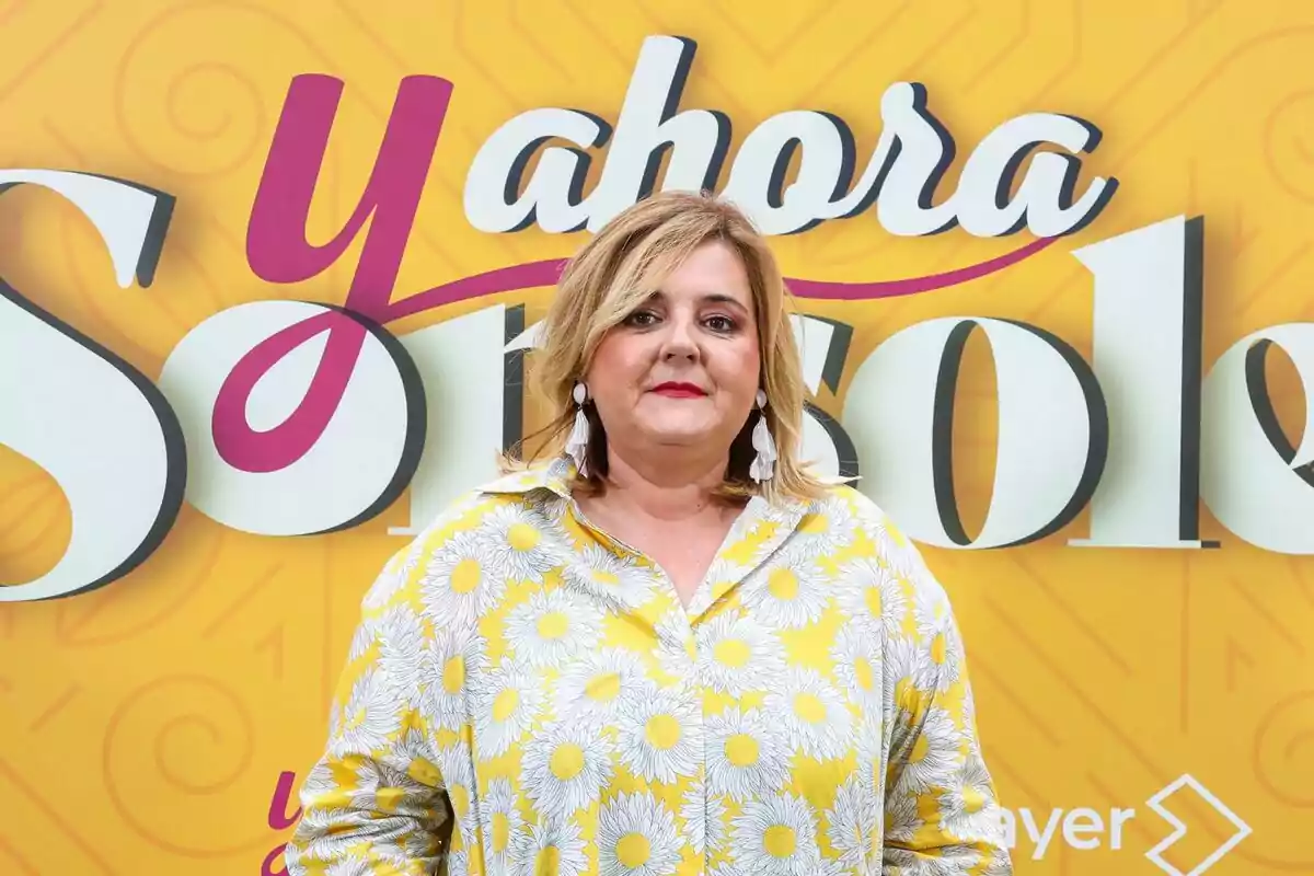Pilar Vidal con blusa amarilla de margaritas posando frente a un cartel amarillo con el texto Pilar Vidal con blusa amarilla de margaritas posando frente a un cartel amarillo con el texto