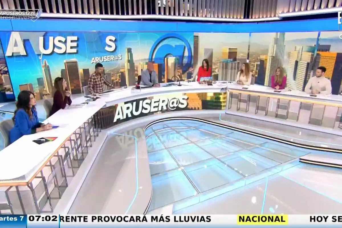 Un grup de col·laboradors com Tatiana Arús, Marc Redondo, Alfons Arús, Angie Cárdenas o Hans Arús està assegut al voltant d'una taula en un set de televisió amb un fons de ciutat i el logotip de “ARUSER@S”.