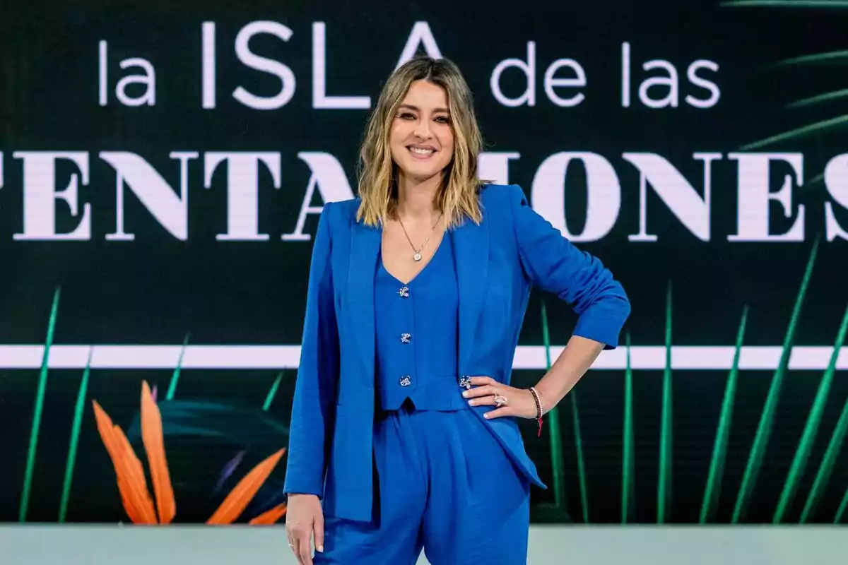 Sandra Barneda sonriendo con traje azul frente a un cartel que dice Sandra Barneda sonriendo con traje azul frente a un cartel que dice