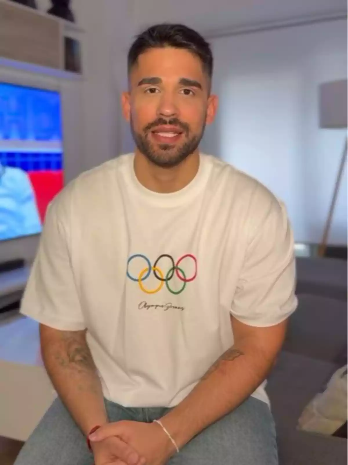 Miguel Frigenti está sentado en una sala, vistiendo una camiseta blanca con el logo de los anillos olímpicos.