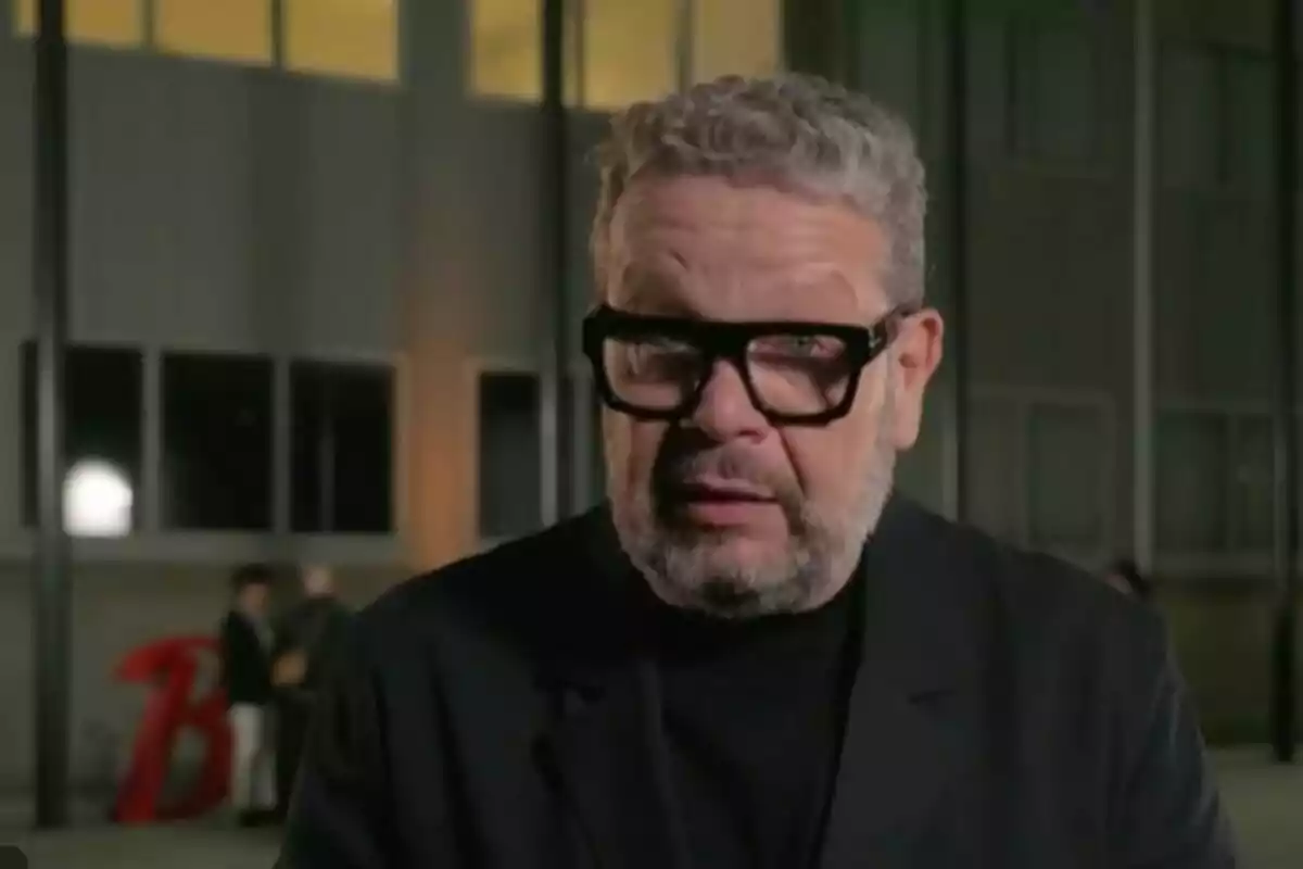 Alberto Chicote amb ulleres negres i barba està dret davant d'un edifici il·luminat a la nit.