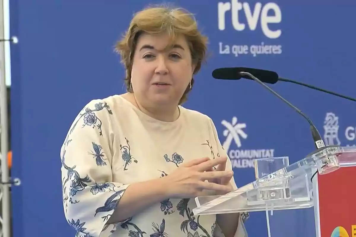 Fotografía de Concepción Cascajosa hablando en un podio con un fondo azul que tiene el logotipo de RTVE y del Benidorm Fest Fotografía de Concepción Cascajosa hablando en un podio con un fondo azul que tiene el logotipo de RTVE y del Benidorm Fest