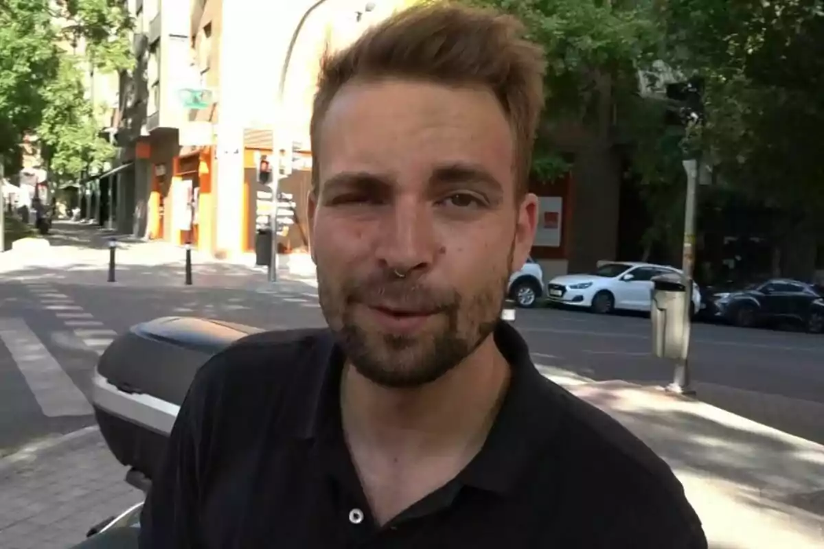 José María Almoguera con camiseta negra está parado en una calle urbana con edificios y árboles al fondo. José María Almoguera con camiseta negra está parado en una calle urbana con edificios y árboles al fondo.