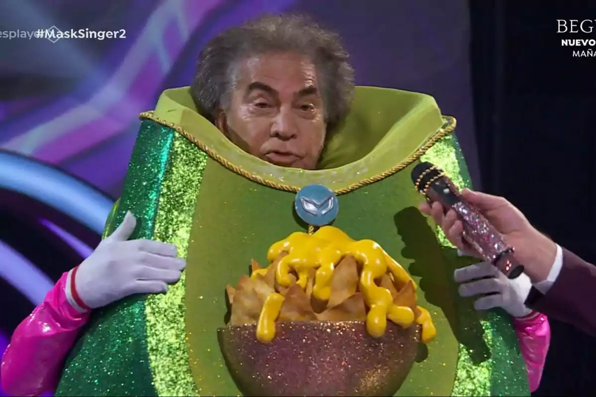 José Luis Rodríguez, El Puma, disfrazada con un traje verde brillante que parece un plato de nachos con queso, sosteniendo un micrófono, en Mask Singer. José Luis Rodríguez, El Puma, disfrazada con un traje verde brillante que parece un plato de nachos con queso, sosteniendo un micrófono, en Mask Singer.