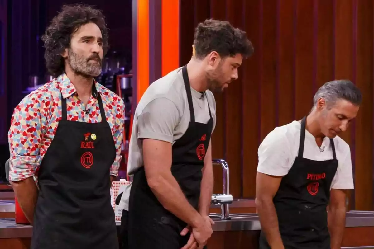 Raúl Gómez, José Lamuño y Pitingo con delantales negros están de pie en una cocina de MasterChef Celebrity. Raúl Gómez, José Lamuño y Pitingo con delantales negros están de pie en una cocina de MasterChef Celebrity.