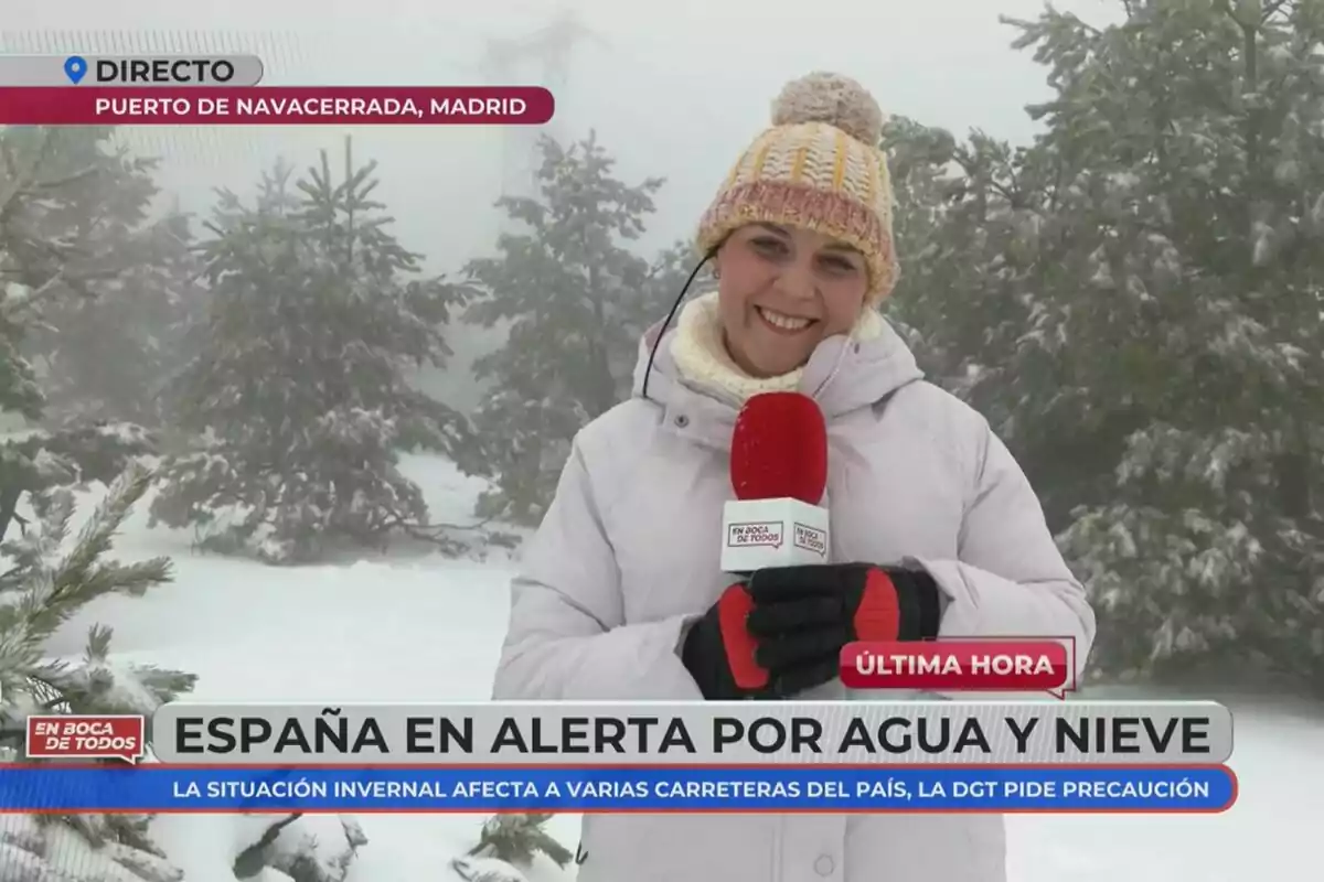 Reportera en el Puerto de Navacerrada, Madrid, informando sobre la alerta en España por agua y nieve, con un fondo de árboles nevados y un micrófono rojo de En Boca de Todos en mano. Reportera en el Puerto de Navacerrada, Madrid, informando sobre la alerta en España por agua y nieve, con un fondo de árboles nevados y un micrófono rojo de En Boca de Todos en mano.