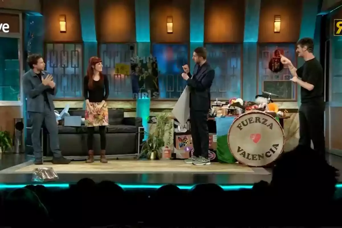 David Broncano, Álvaro Cervantes y Miriam Garlo están en un escenario de un programa de televisión con decoraciones coloridas y un tambor que dice David Broncano, Álvaro Cervantes y Miriam Garlo están en un escenario de un programa de televisión con decoraciones coloridas y un tambor que dice