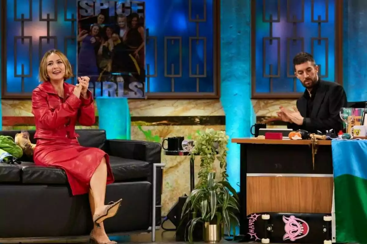 Rigoberta Bandini con un vestido rojo está sentada en un sofá negro mientras David Broncano aplaude desde un escritorio en La Revuelta. Rigoberta Bandini con un vestido rojo está sentada en un sofá negro mientras David Broncano aplaude desde un escritorio en La Revuelta.