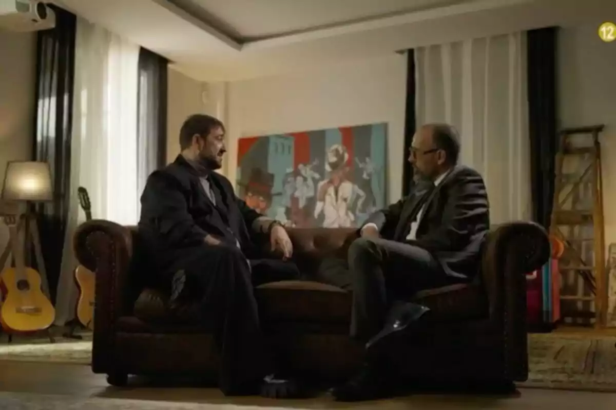 Antonio Orozco y Risto Mejide sentados en un sofá de cuero en una sala de estar, conversando frente a un cuadro colorido; hay guitarras y una lámpara en el fondo.