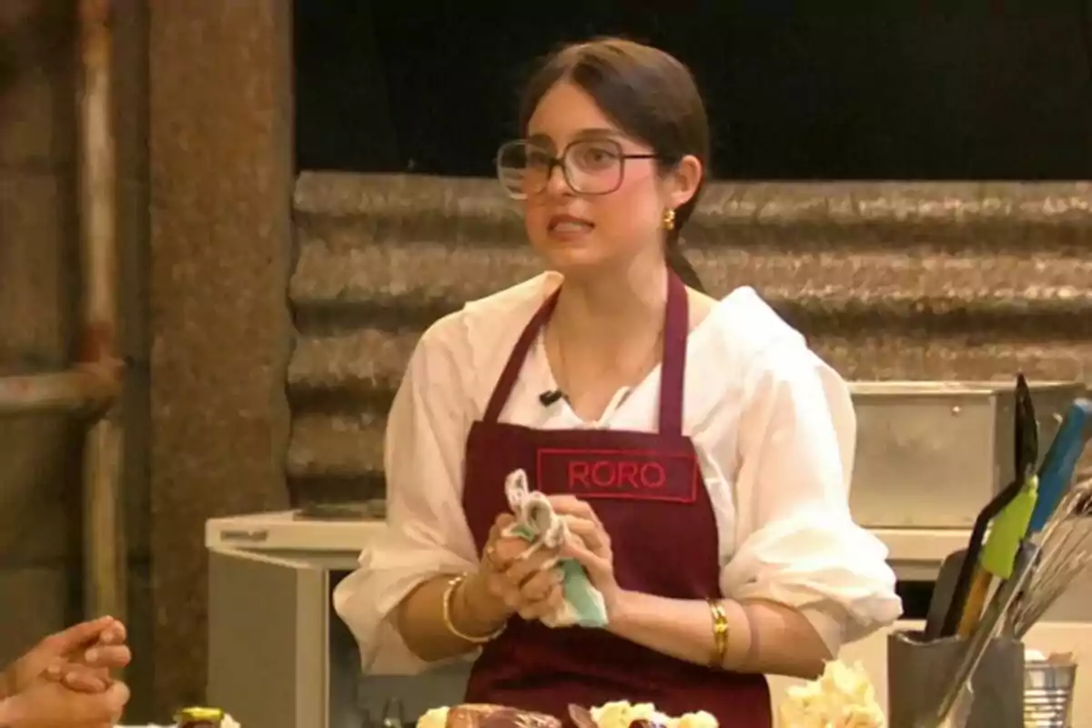 Roro amb ulleres i davantal vermell està en una cuina sostenint un drap a Next Level Chef.