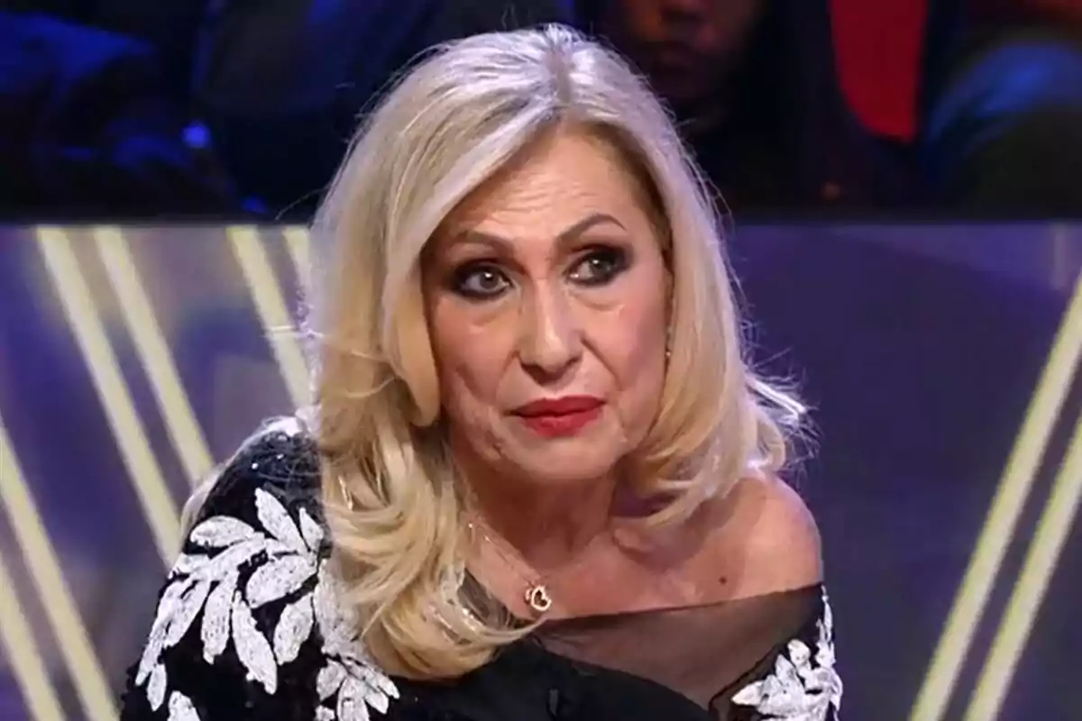 Rosa Benito de cabello rubio y vestido negro con detalles blancos está sentada en De Viernes. Rosa Benito de cabello rubio y vestido negro con detalles blancos está sentada en De Viernes.