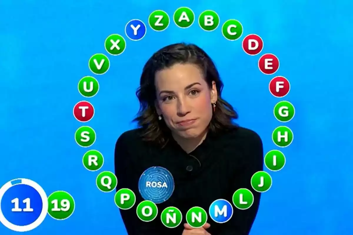 Rosa participando en Pasapalabra con letras del abecedario en un círculo a su alrededor y un marcador de tiempo en la esquina inferior izquierda.