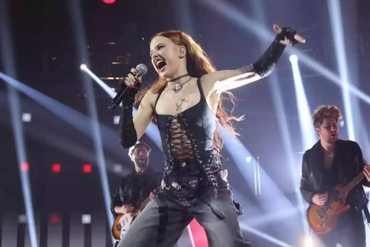 Ruslana vestida de negro, cantando enérgicamente en el ptó de OT 2023. De fondo, dos guitarristas. Ruslana vestida de negro, cantando enérgicamente en el ptó de OT 2023. De fondo, dos guitarristas.
