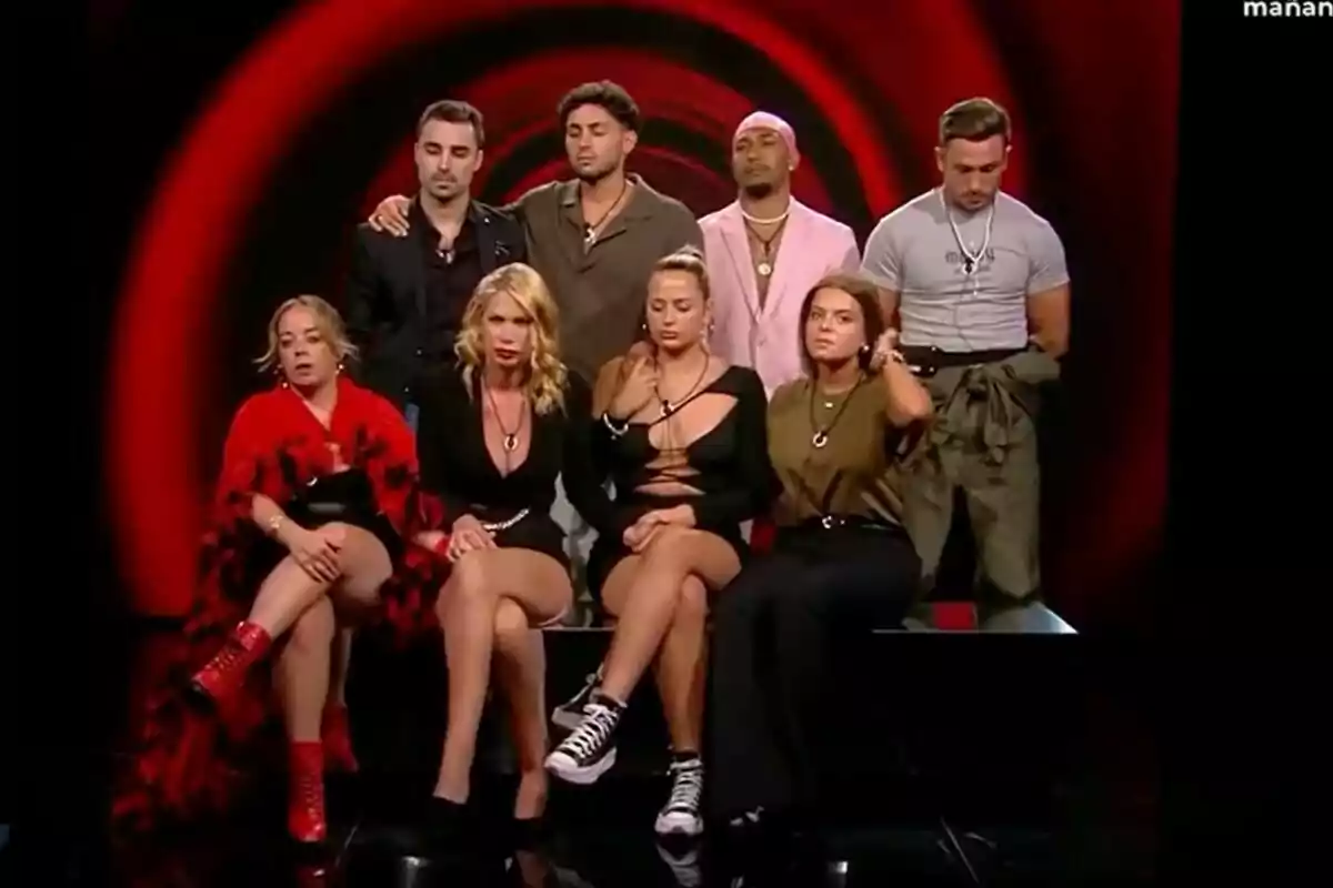 Maica, Maite, Elsa, Adrián, Jorge, Vanessa, Manu, Juan i Laura Galera estan asseguts i drets davant d'un fons vermell i negre, amb expressions serioses i vestimenta variada a Gran Hermano. Maica, Maite, Elsa, Adrián, Jorge, Vanessa, Manu, Juan i Laura Galera estan asseguts i drets davant d'un fons vermell i negre, amb expressions serioses i vestimenta variada a Gran Hermano.