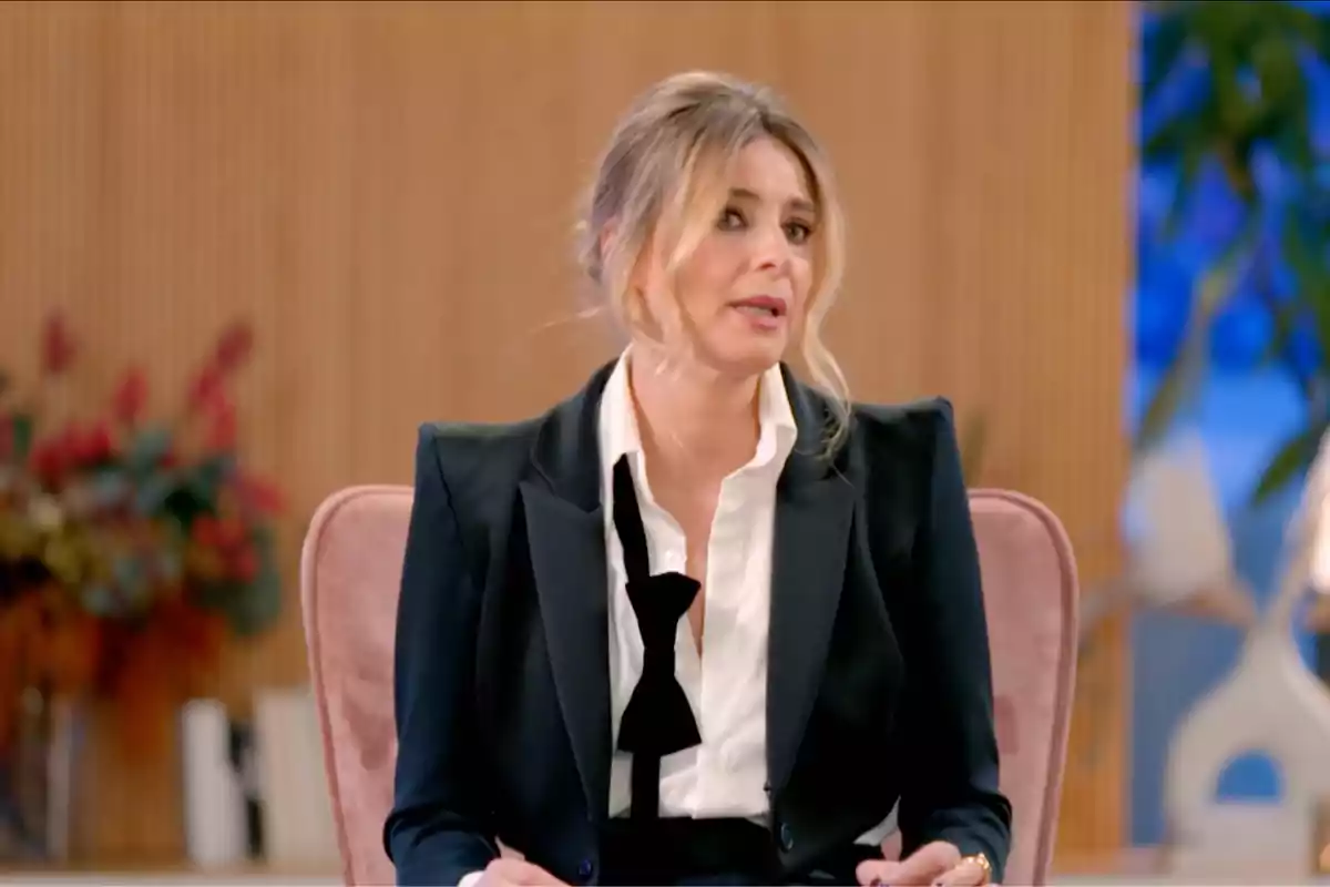 Sandra Barneda sentada en una silla, vestida con un traje formal, en un entorno interior con decoración de fondo. Sandra Barneda sentada en una silla, vestida con un traje formal, en un entorno interior con decoración de fondo.
