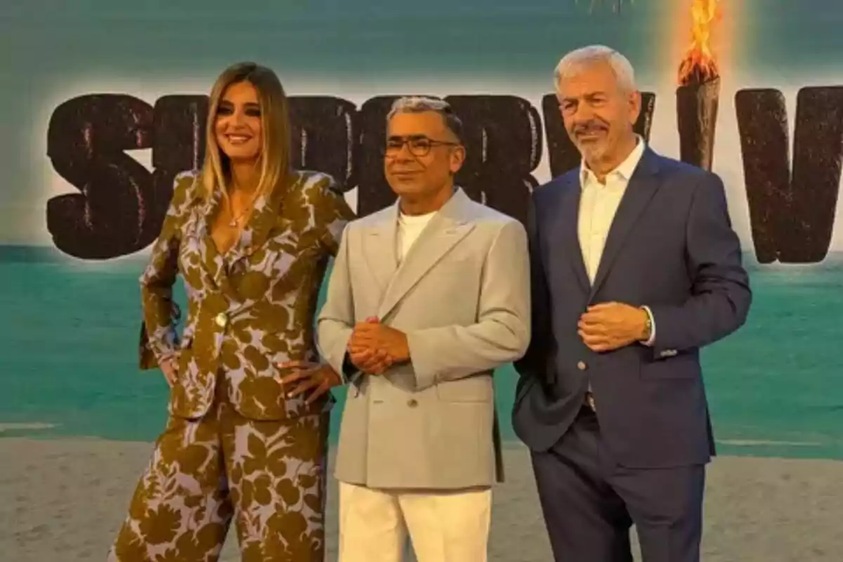Sandra Barneda, Jorge Javier Vázquez i Carlos Sobera posen davant d'un cartell amb lletres grans de Supervivientes amb una torxa encesa.