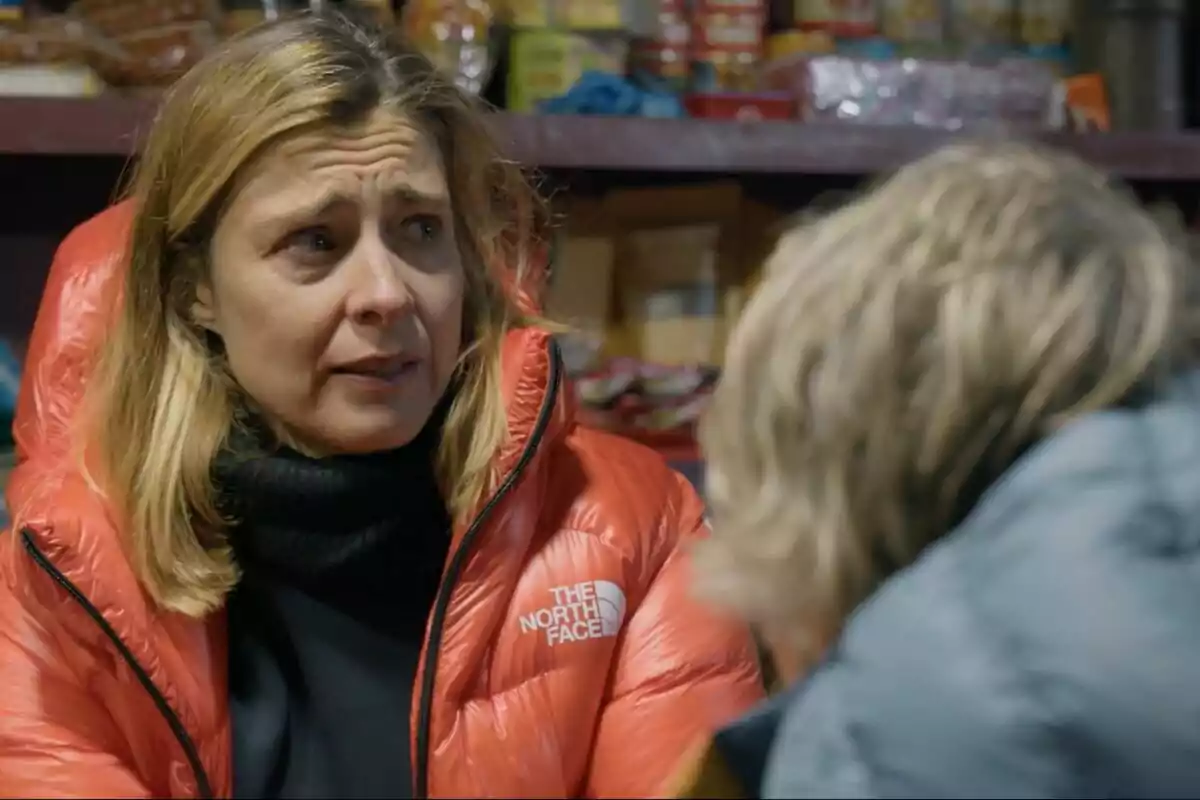 Sandra Barneda con chaqueta roja de The North Face parece preocupada mientras habla con Jesús Calleja en un entorno interior con estantes llenos de productos en Universo Calleja. Sandra Barneda con chaqueta roja de The North Face parece preocupada mientras habla con Jesús Calleja en un entorno interior con estantes llenos de productos en Universo Calleja.