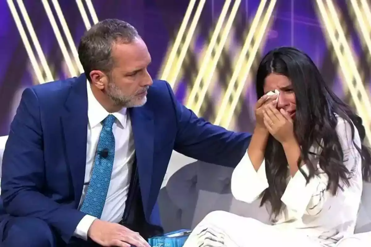 Santi Acosta en traje azul consuela a Isa Pantoja que llora mientras se limpia las lágrimas con un pañuelo en De Viernes. Santi Acosta en traje azul consuela a Isa Pantoja que llora mientras se limpia las lágrimas con un pañuelo en De Viernes.