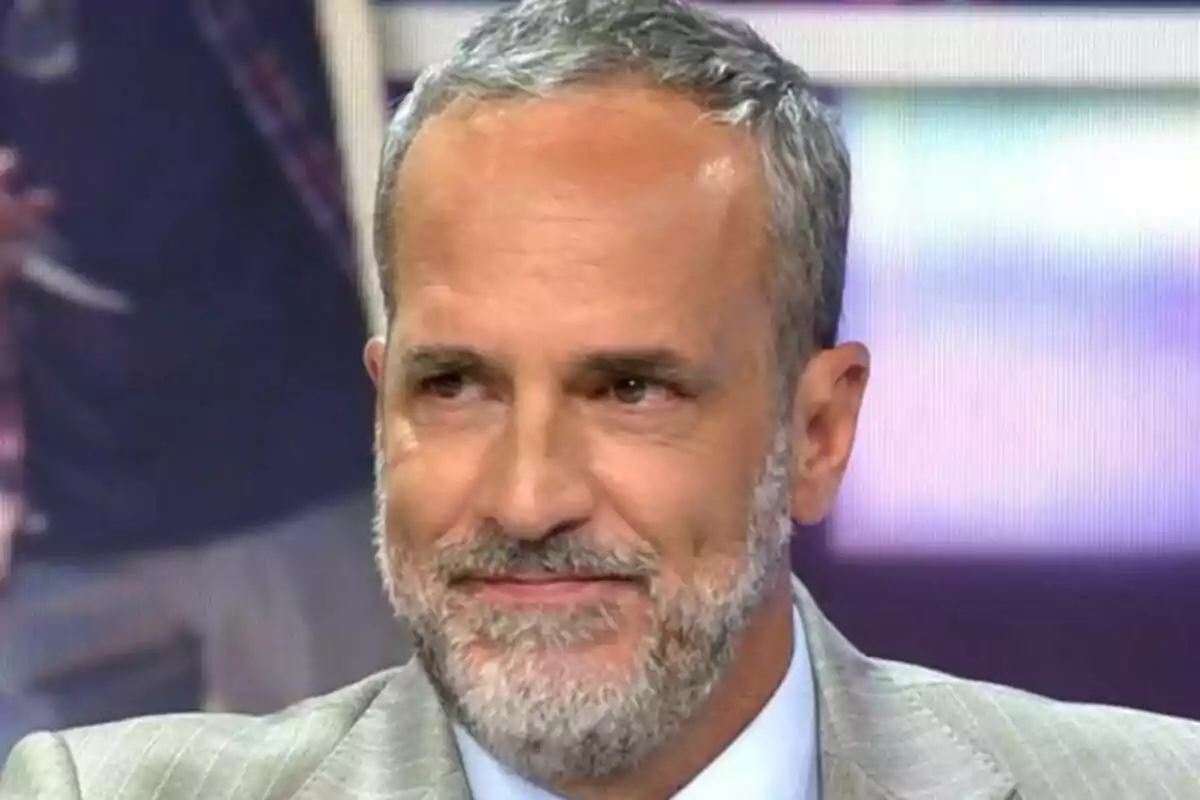 Santi Acosta de cabello canoso y barba, vestido con traje claro, emocionado en el plató de De Viernes
