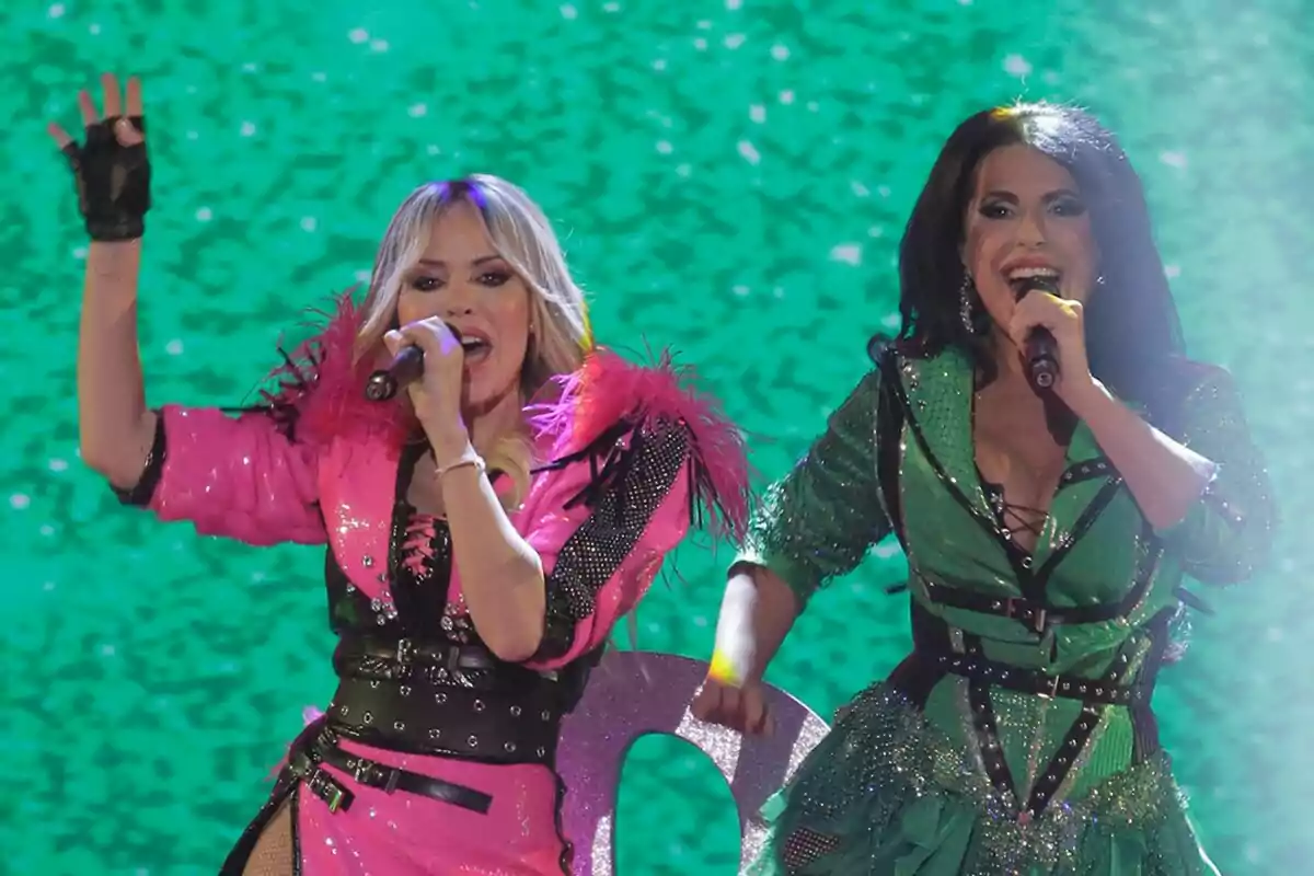 Sonia y Selena cantando en el escenario con trajes brillantes del Benidorm Fest, una en rosa y la otra en verde, sobre un fondo verde. Sonia y Selena cantando en el escenario con trajes brillantes del Benidorm Fest, una en rosa y la otra en verde, sobre un fondo verde.